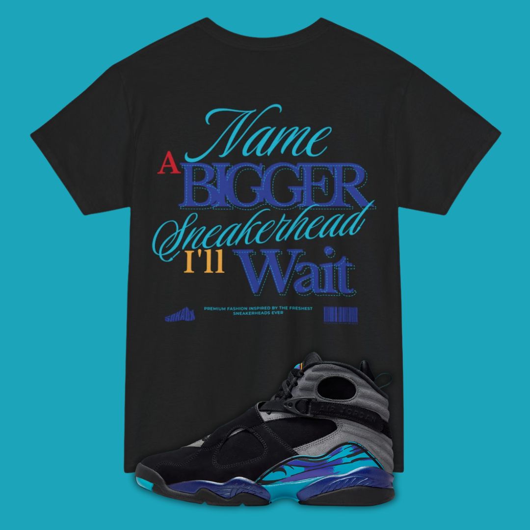 Black view of a typography t-shirt with colorful text Name a Bigger Sneakerhead I'll Wait and a pair of sneakers on a blue background