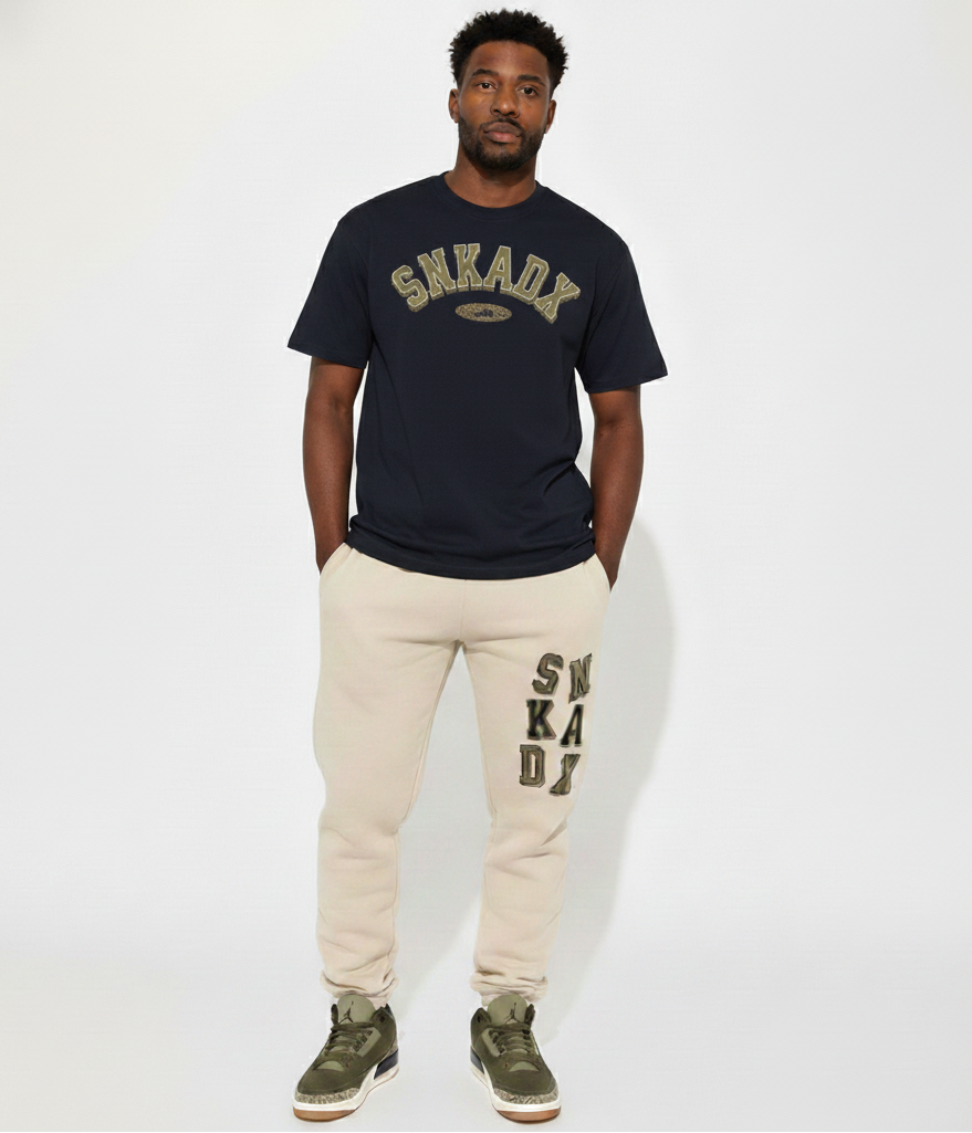 Man wearing a black 'SNKADX' t-shirt and beige pants with 'SNKADX' logo on a white background
