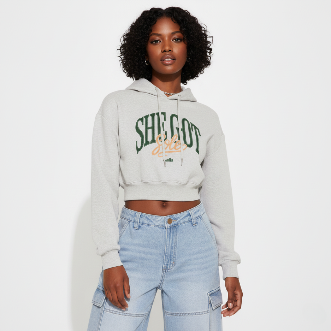 Woman wearing a light gray hoodie with She Got Sole text and light blue jeans on a white background