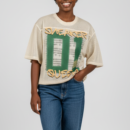 Person wearing a beige t-shirt with graphic design and blue jeans on a white background