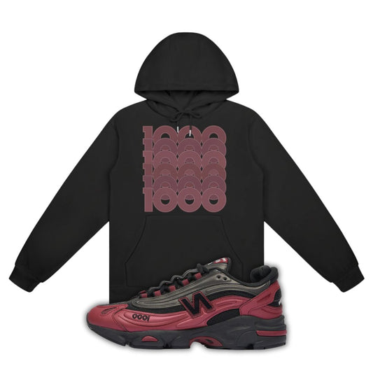 Black hoodie with red graphic design and a red and black New Balance 1000 Monarch Burgundy sneaker on a white background