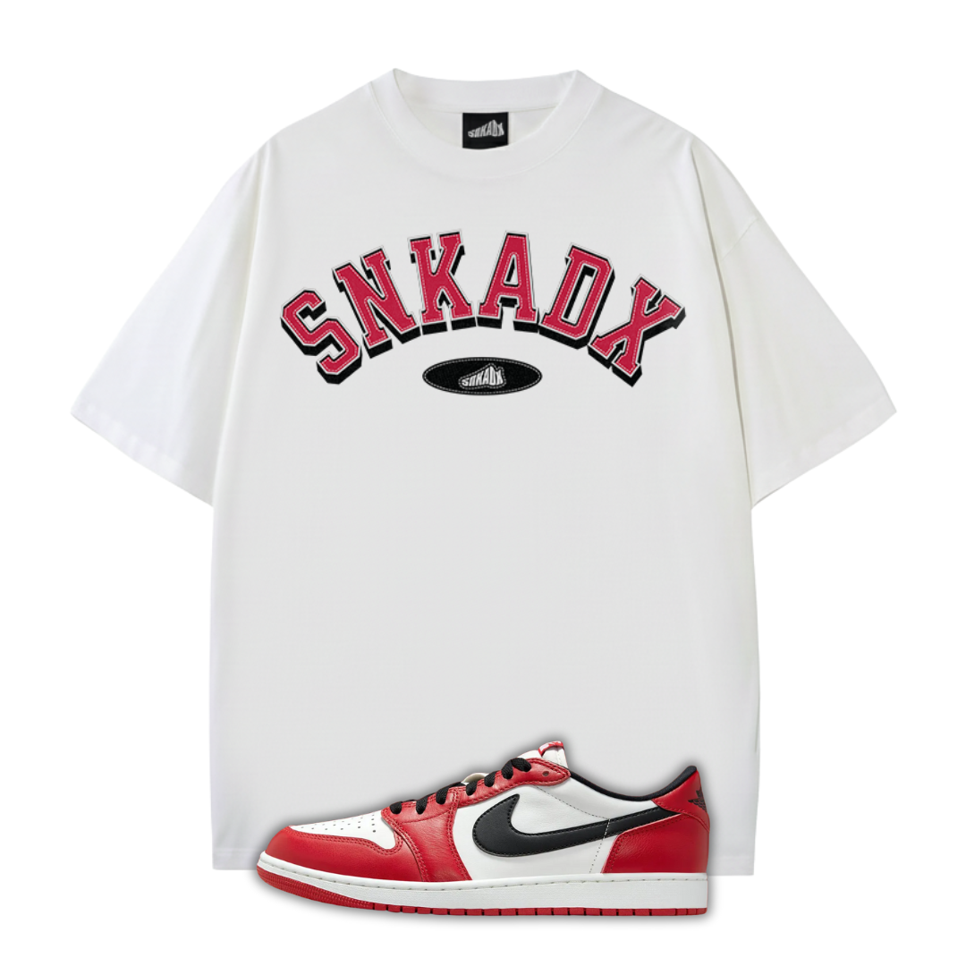 White t-shirt with 'SNKADX' text and a Jordan 1 Chicago sneaker on a white background