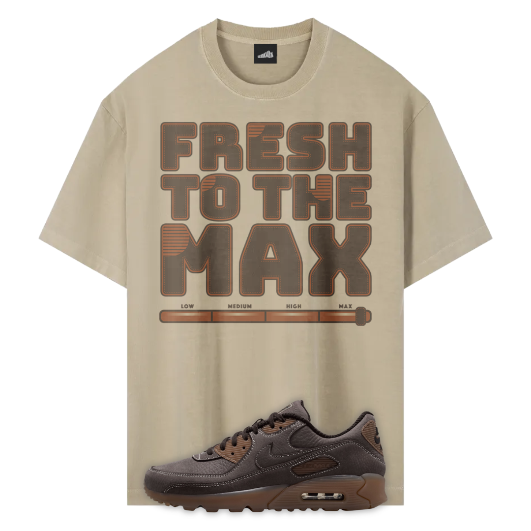 A beige graphic T-shirt with the words 'FRESH TO THE MAX' in large brown block letters and a horizontal progress-bar style graphic underneath, shown alongside a dark brown Nike Air Max Shadow Brown sneaker on a white background.
