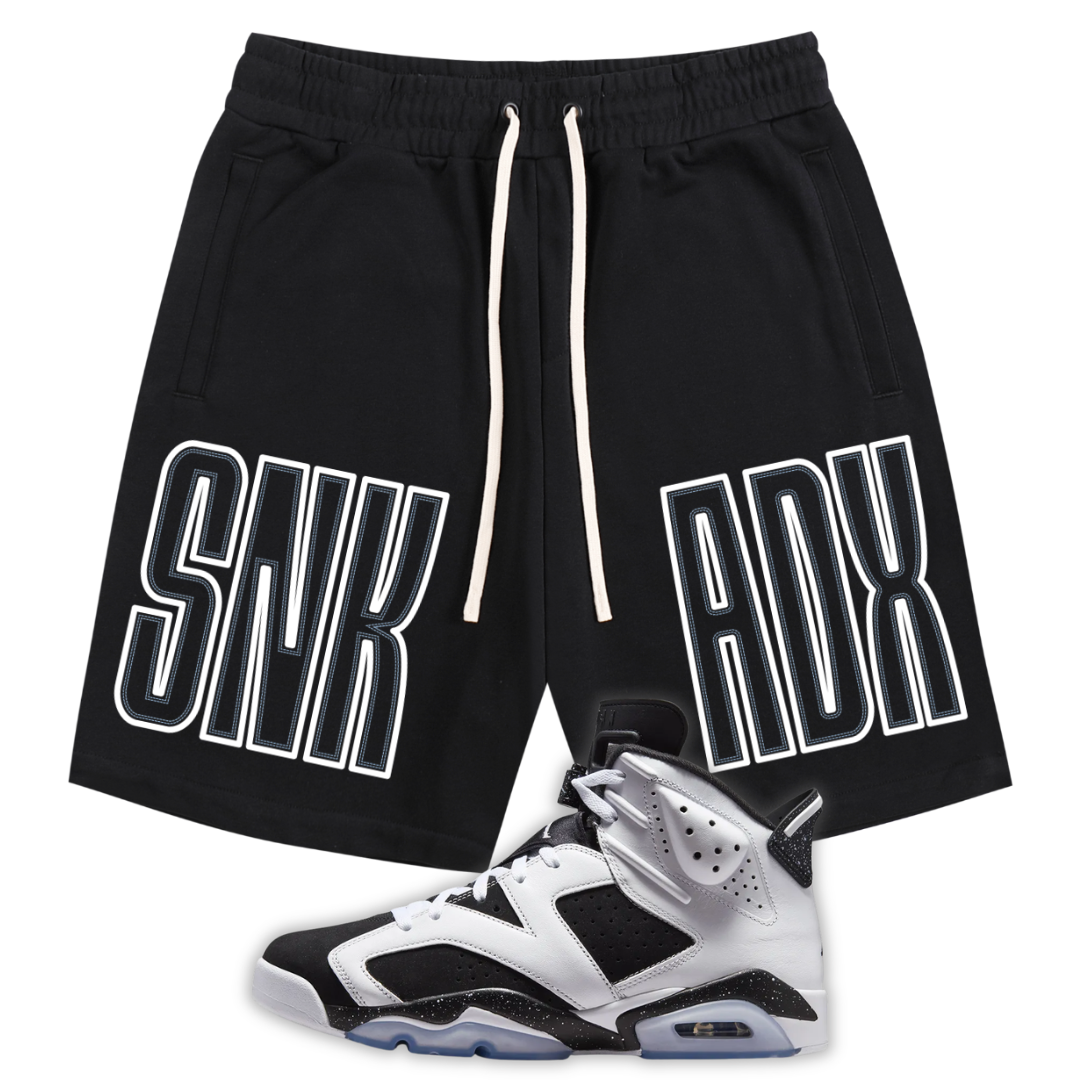 Black athletic shorts with white drawstrings and large white outlined 'SNK ADX' text on the sides, shown with a black, white, and gray Jordan 6 Oreo sneaker on a plain white background.