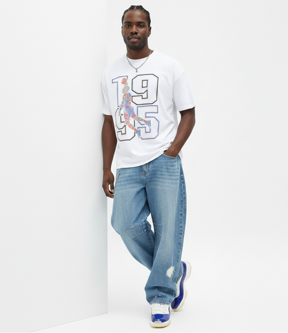 Man wearing a white t-shirt with a graphic design and blue jeans on a white background
