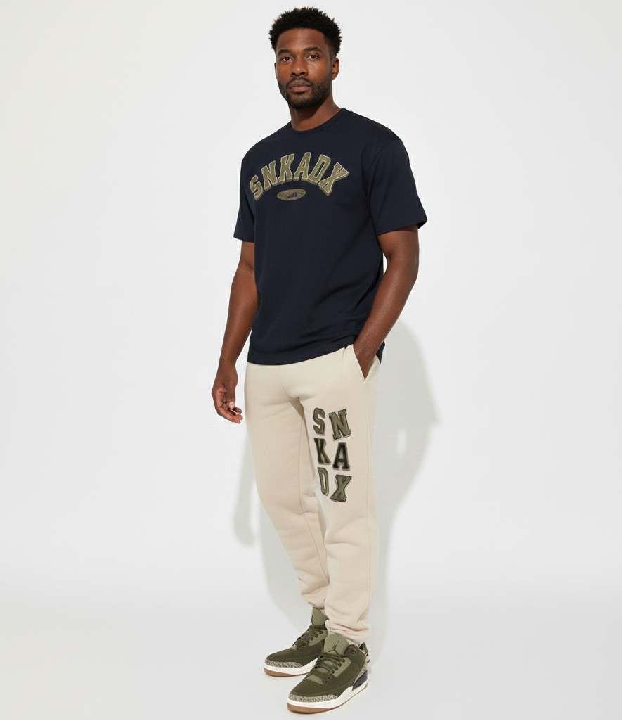 Man wearing black t-shirt and beige sweatpants with 'SNKADX' branding on a white background