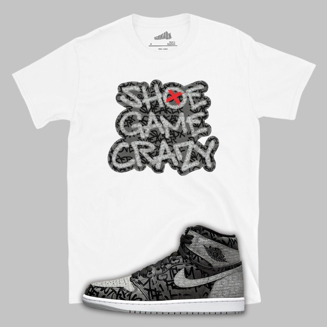 White t-shirt with 'Shoe Game Crazy' graphic and Jordan 1 Rebellionaie shoe design on a gray background