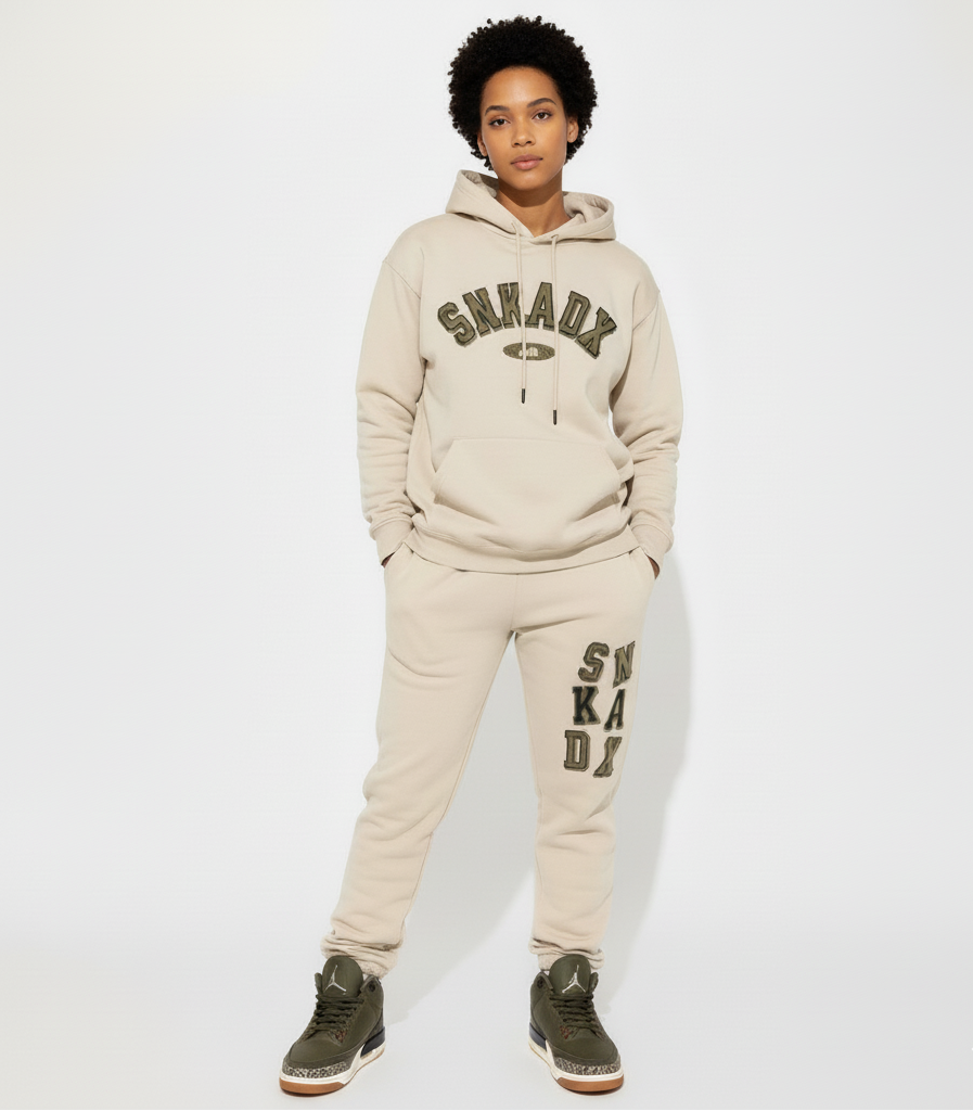 Woman wearing a beige 'SNKADX' tracksuit on a white background